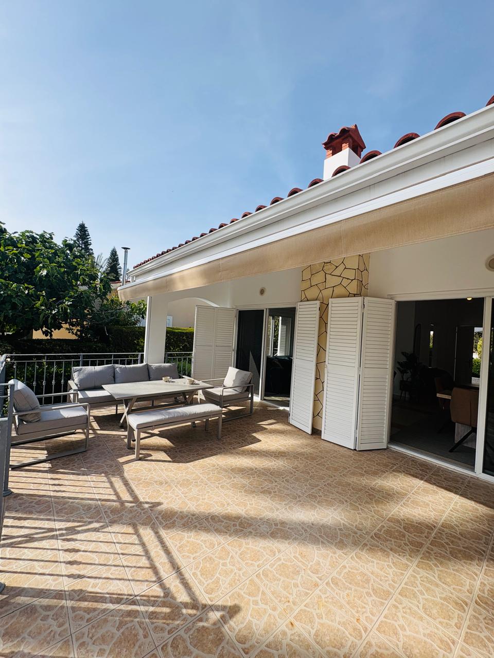 Shaded, large tiled terrace with comfy lounge seating and garden views.