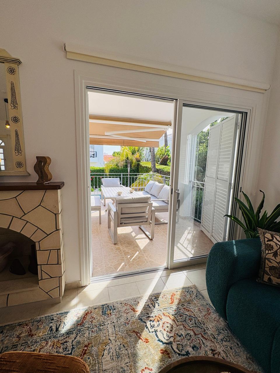 Sunny lounge with terrace seating, awning, and garden views.