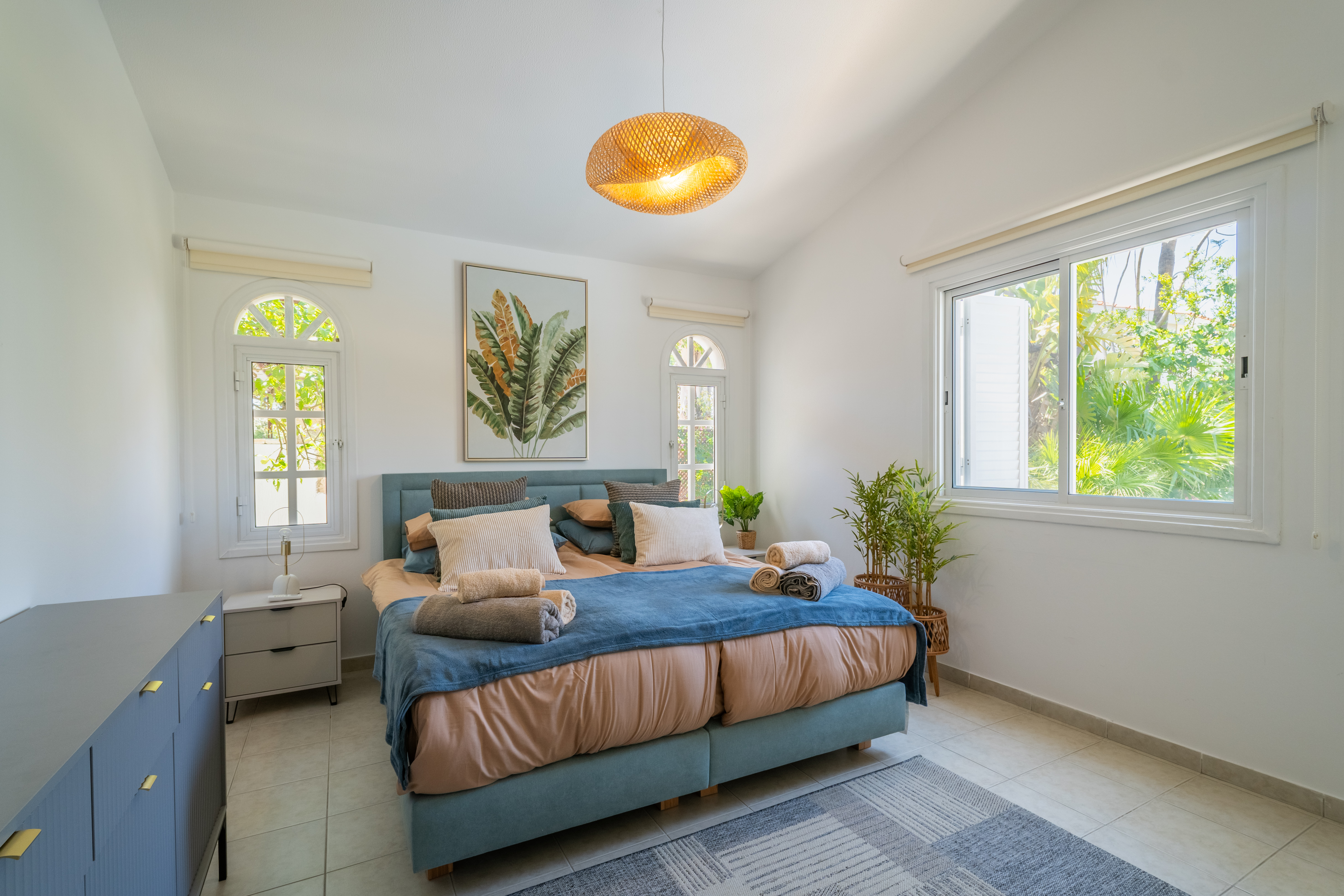 Sunny bedroom with king bed, arched windows, and garden views.