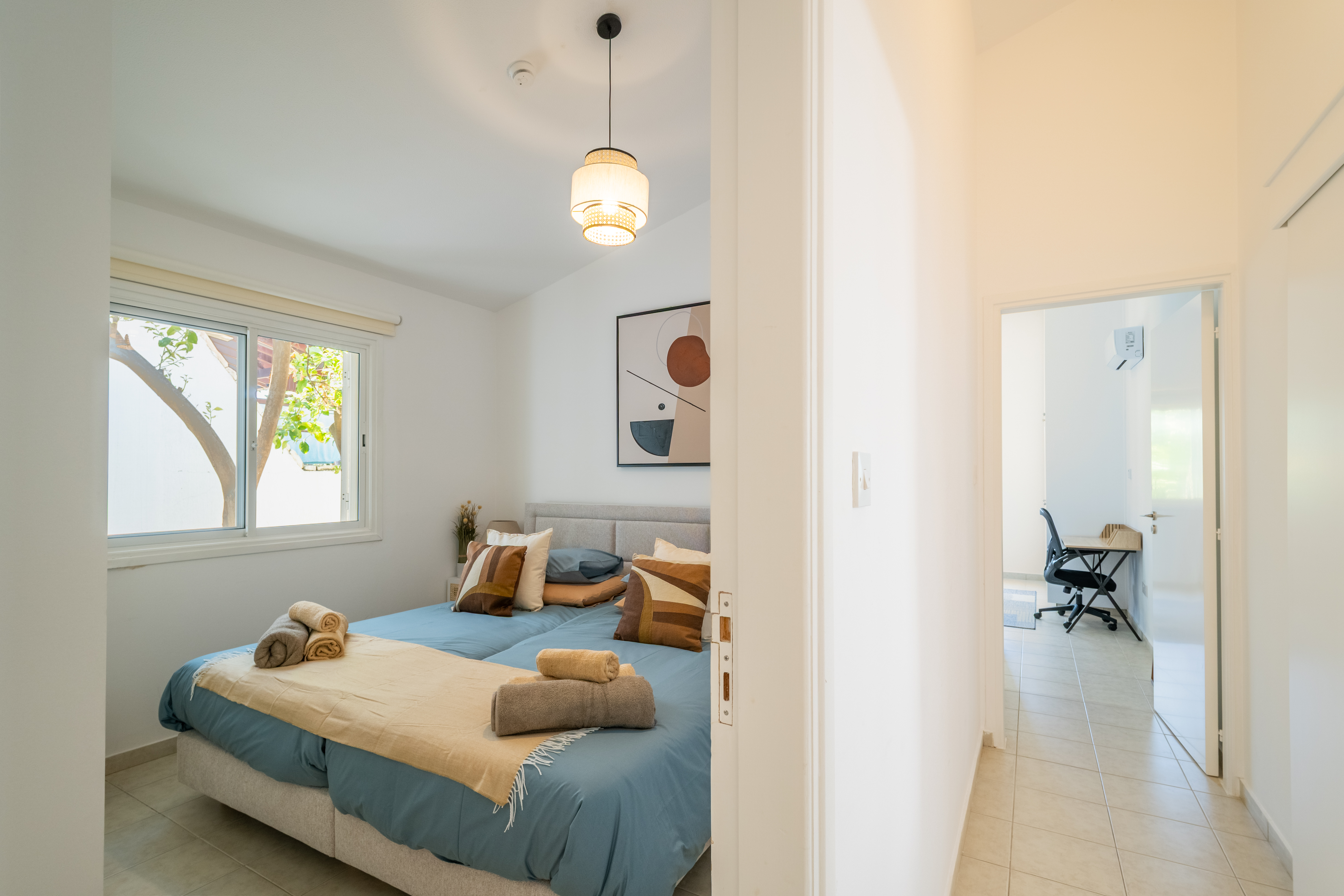 Bright bedroom with comfy bed, garden view, and adjacent workspace/AC.