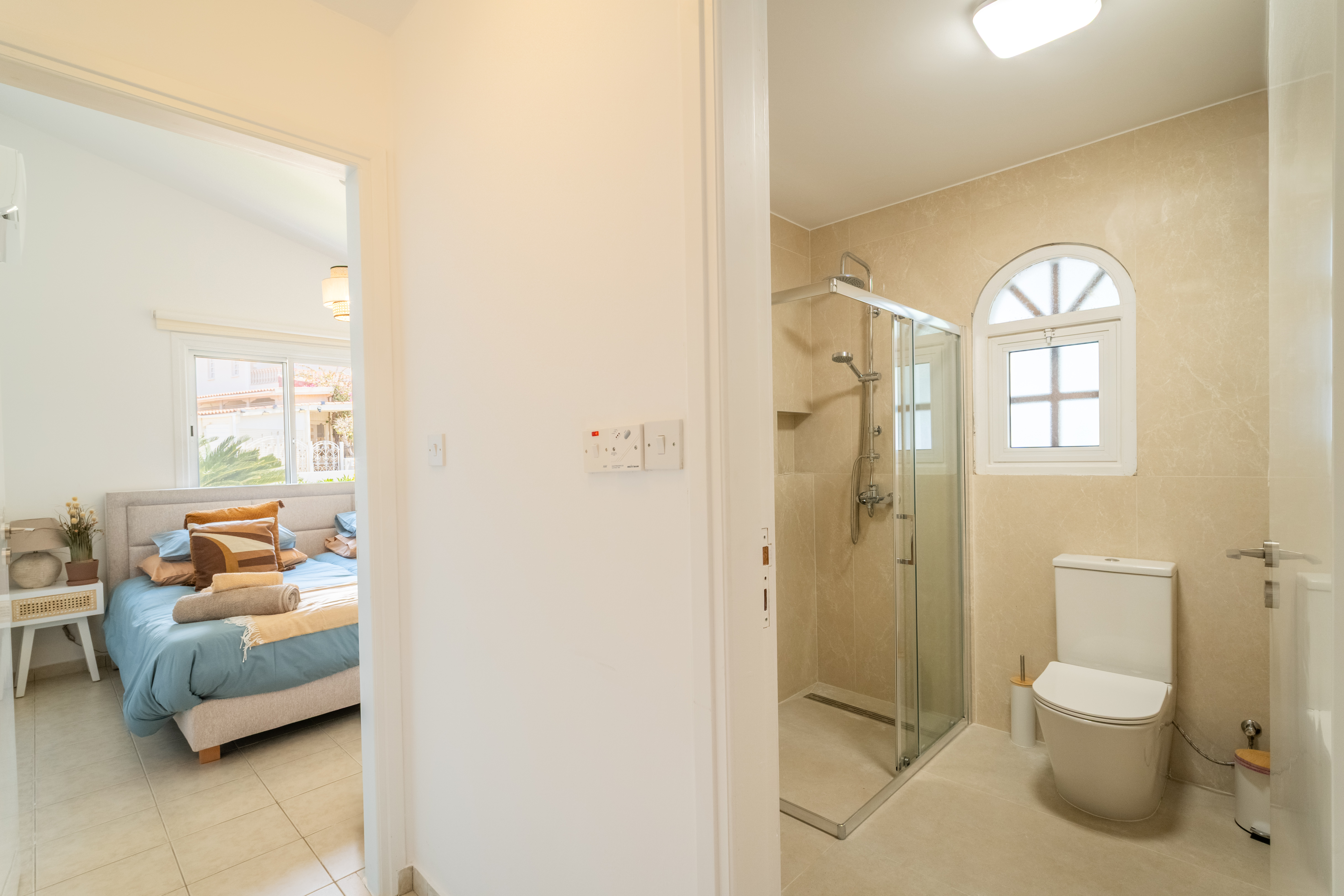 Bright ensuite bathroom with walk-in shower beside a cozy, sunlit bedroom