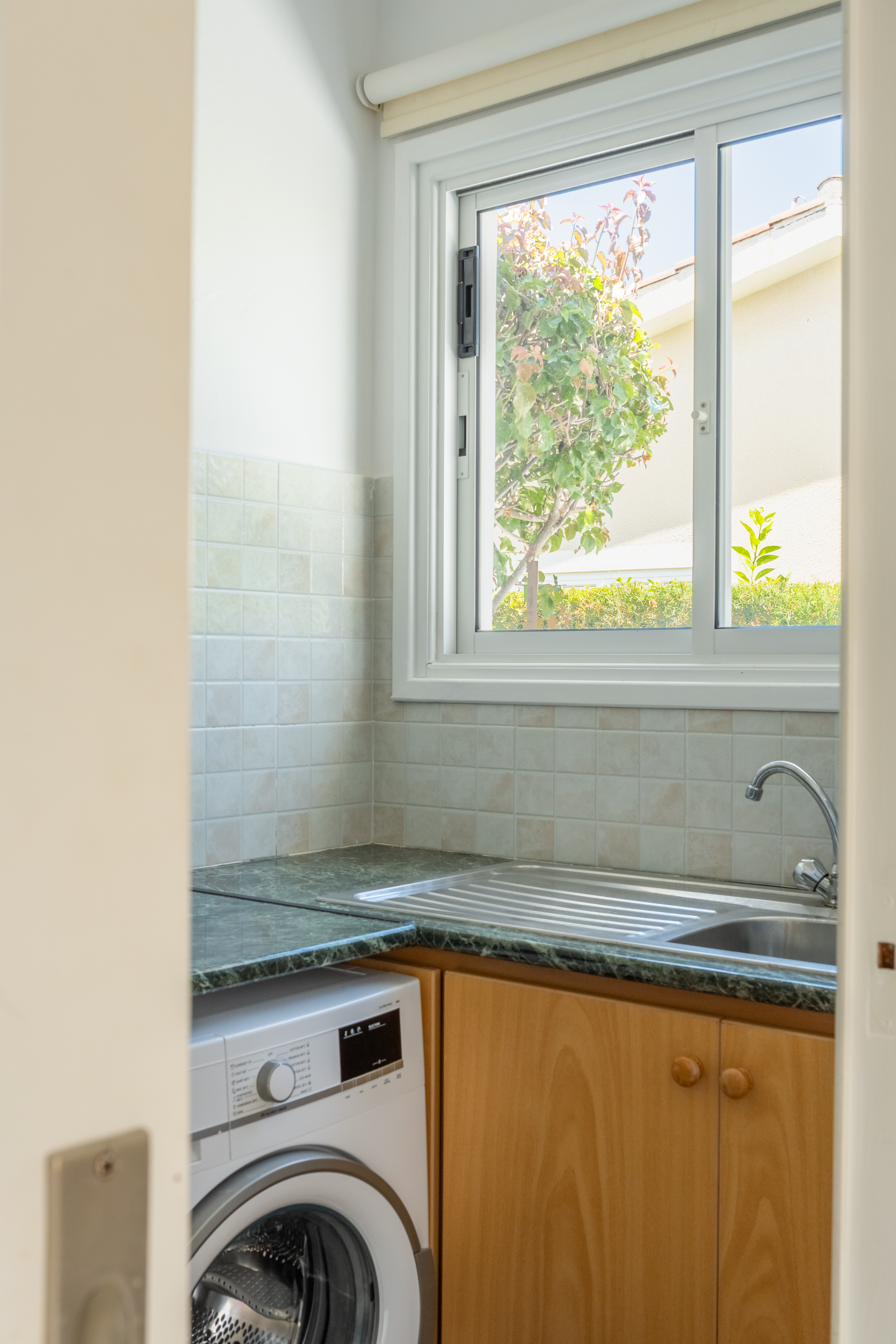 Bright utility nook with washer, sink, and garden-view window.