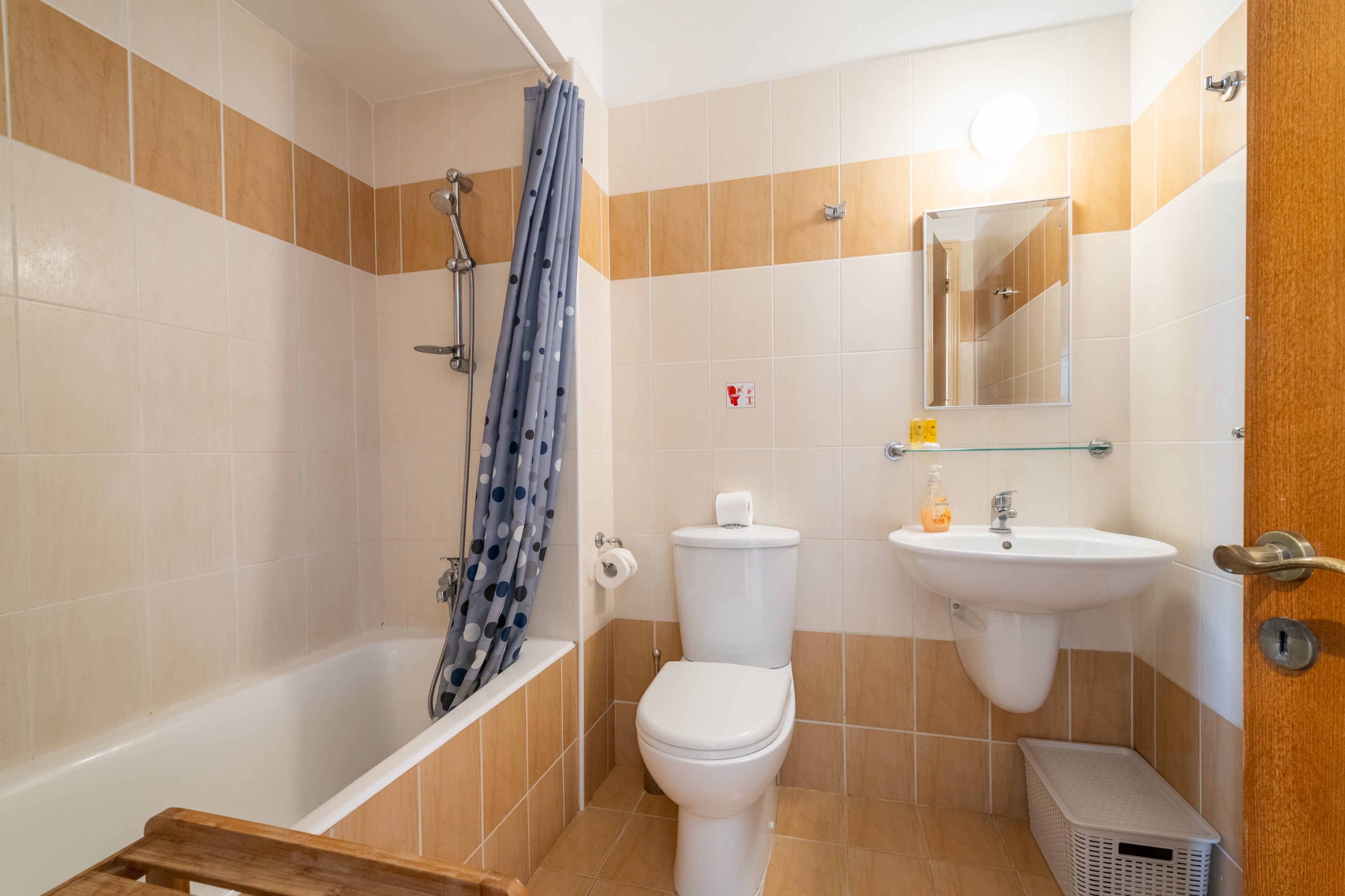 Bright, spotless bathroom with tub/shower, mirror cabinet, and toiletries