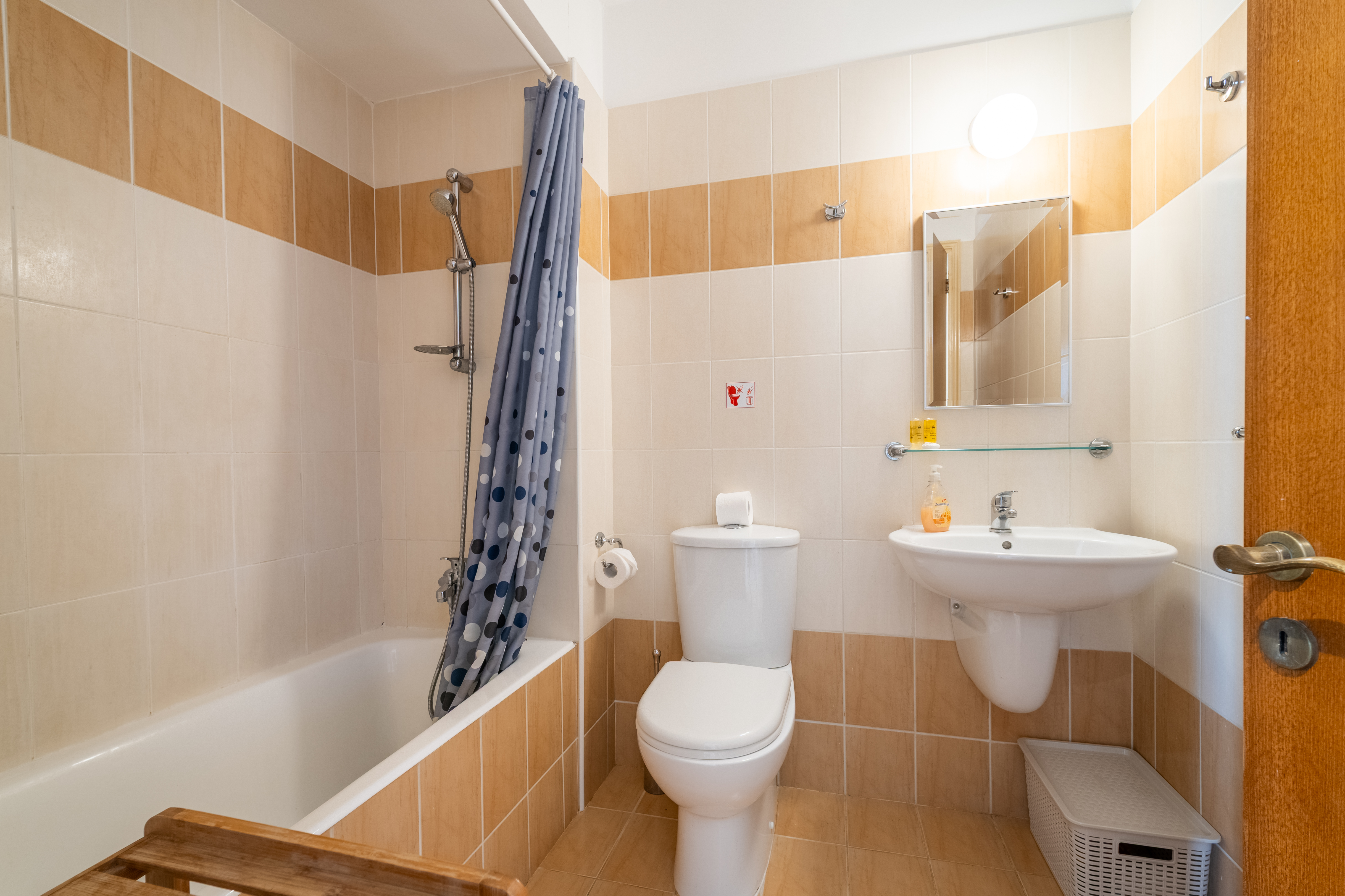Bright, spotless bathroom with tub/shower, mirror cabinet, and toiletries