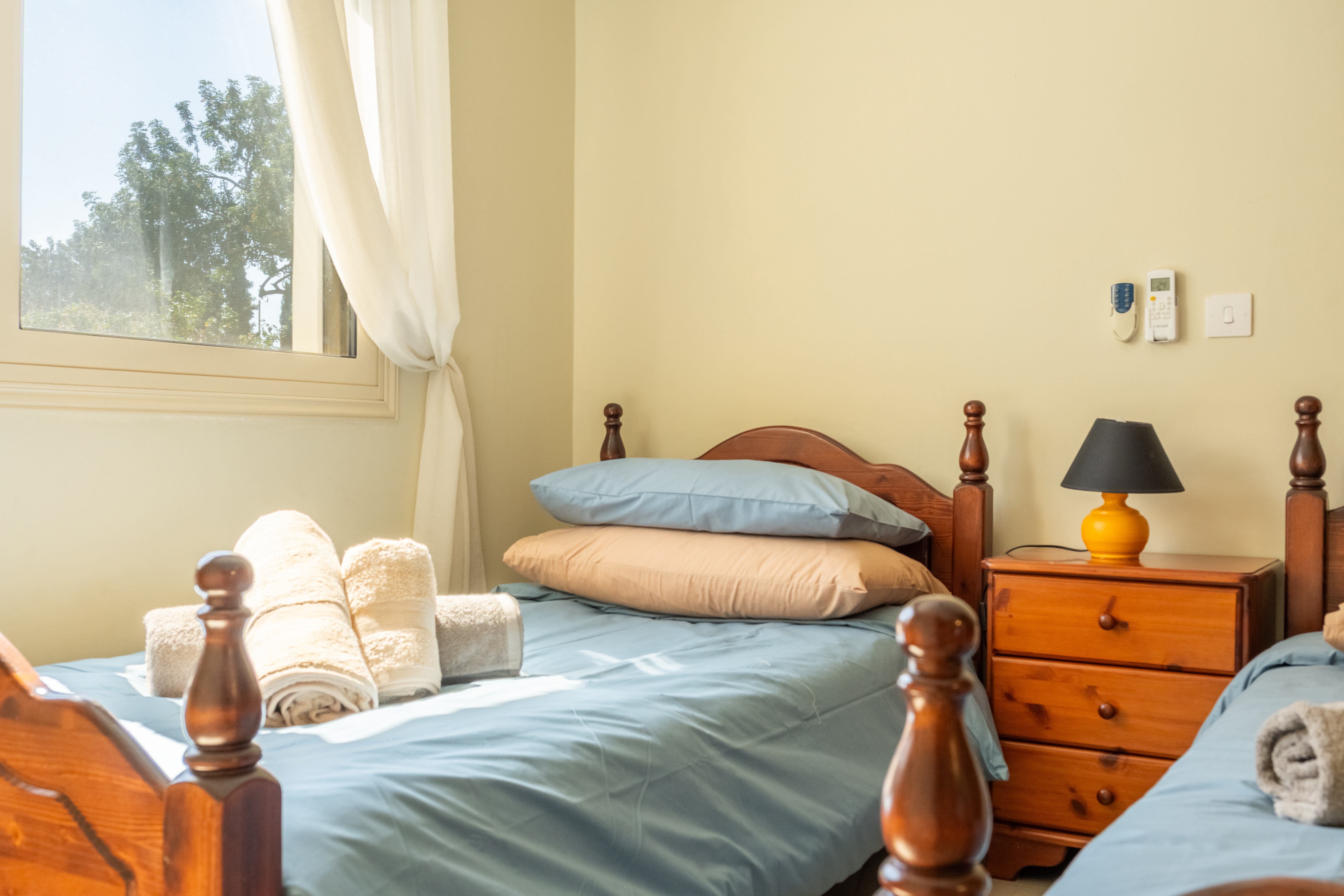 Sunny twin room with fresh linens, window views, and bedside lamp